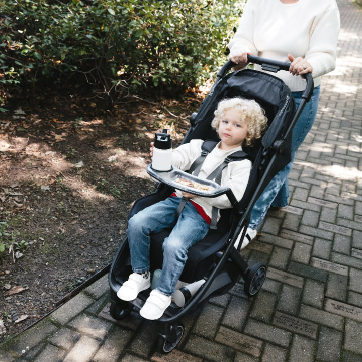 UPPAbaby MINU V3 Jake lightweight stroller with snack tray, toddler seated on outdoor path