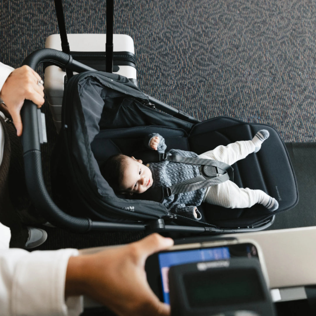 “UPPAbaby MINU V3 Jake lightweight travel stroller with baby reclined, overhead view at airport with luggage”