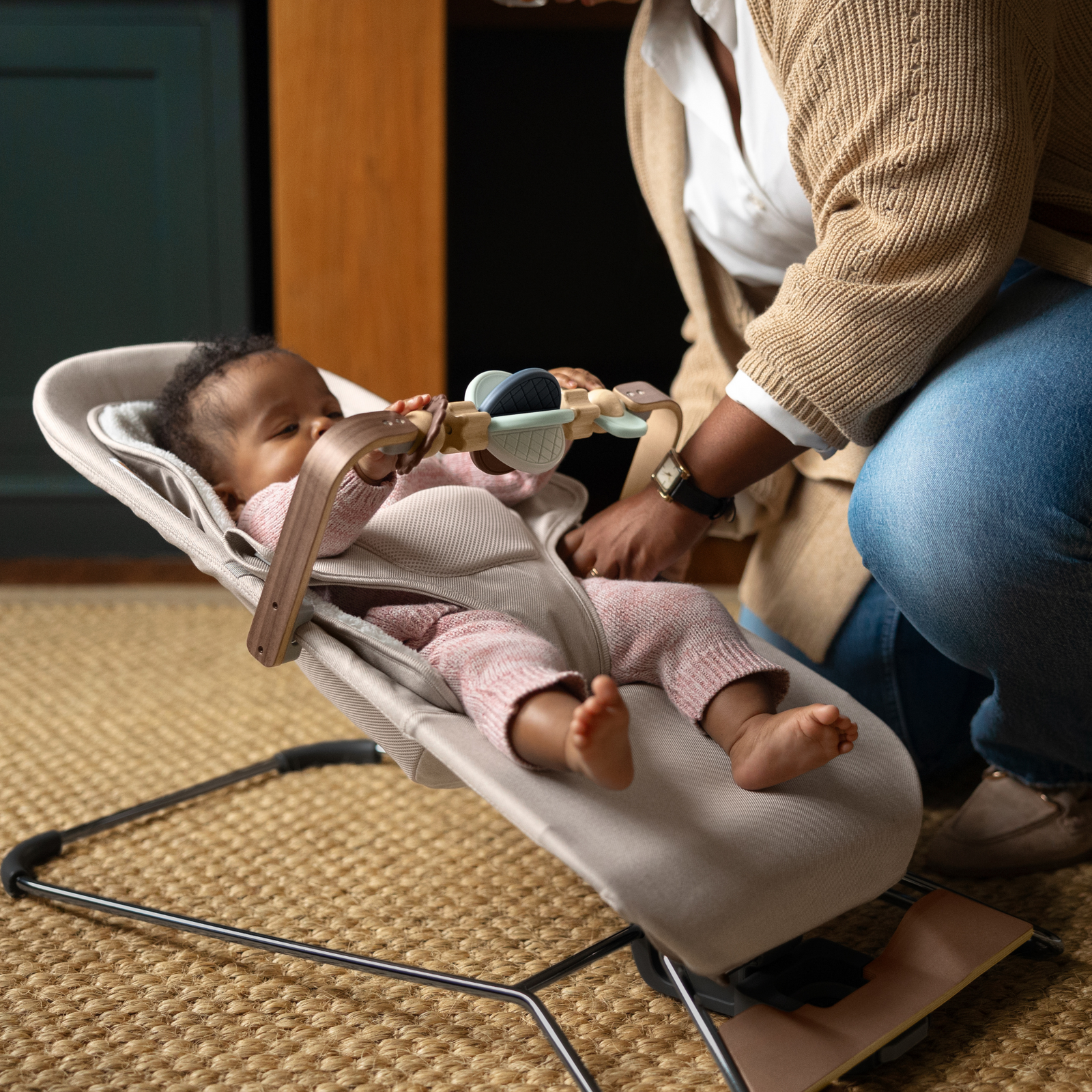 This is a lifestyle shot of a mom attaching the wonder wheel toy bar to the Mira bouncer. The baby is playigng with the toy bar
