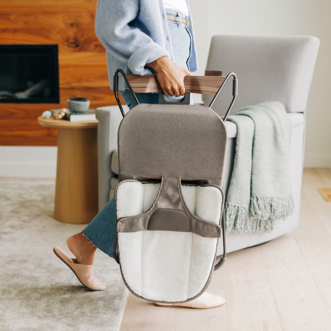 This is a lifestyle shot of a parent moving the Mira bouncer out of the living room with the simple carry handle