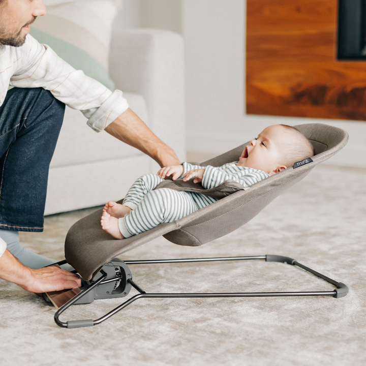 This image shows a dad bouncing his baby in the Mira bouncer on the living room floor