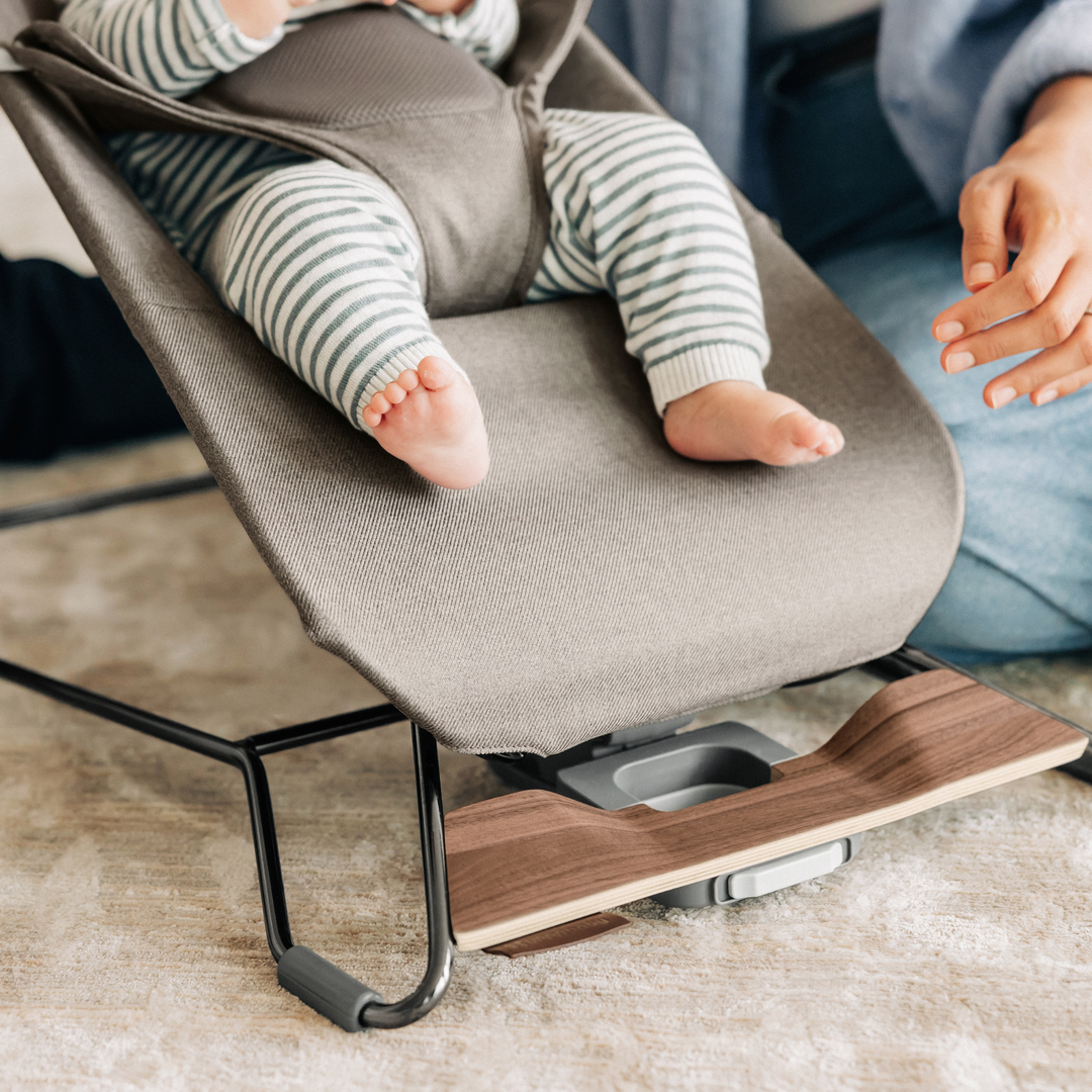 This lifestyle shot is a close up of cute baby feet of a baby in the bouncer and shows the easy carry handle, along with the button for recline adjustment