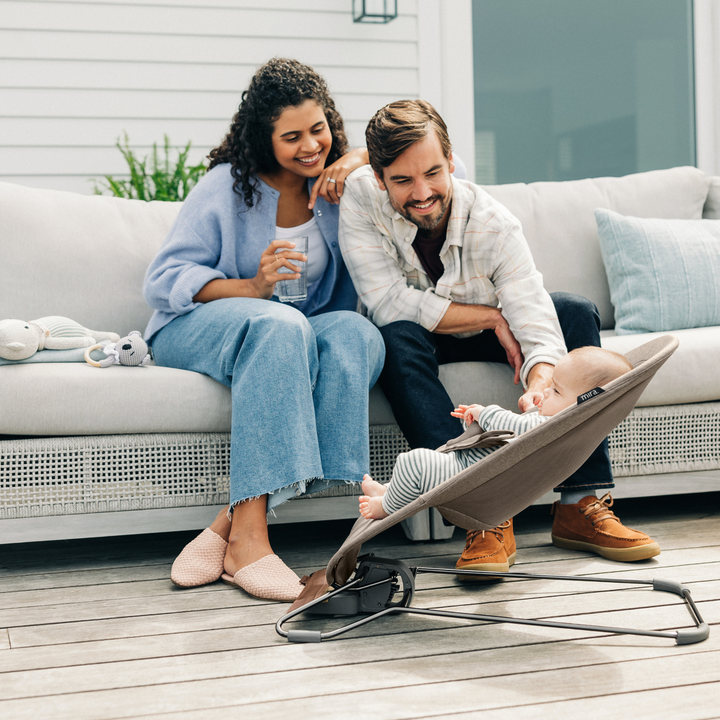 This is an image of two parents sitting on their patio cooing at their baby in the bouncer