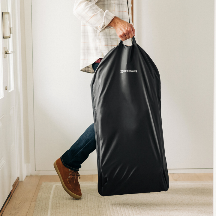 This is an image of a dad walking in a hallway carrying the Mira bouncer in its handy storage bag