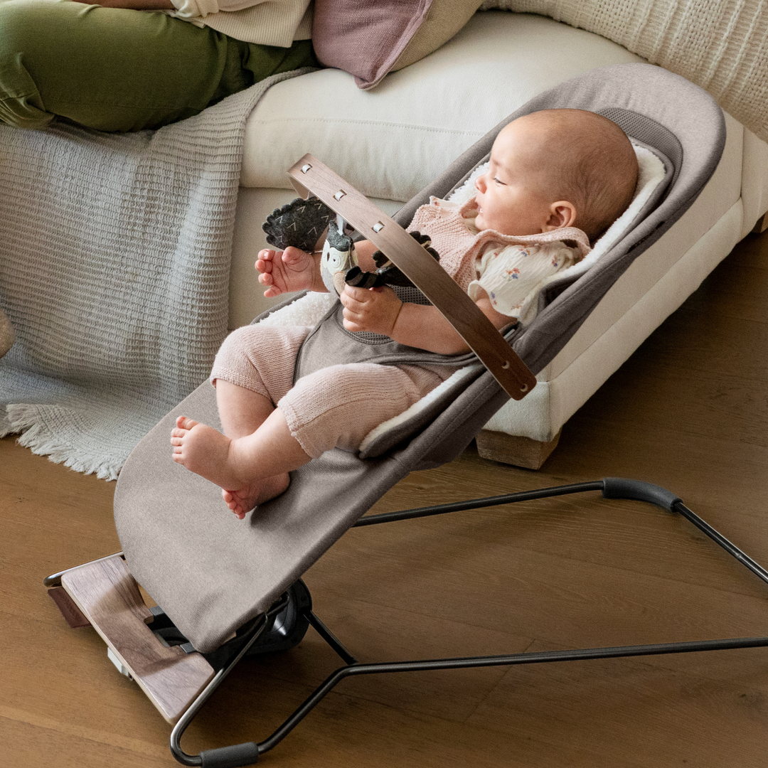 This is a lifestyle shot of a smiling baby in the bouncer playing with the forest fun toy bar