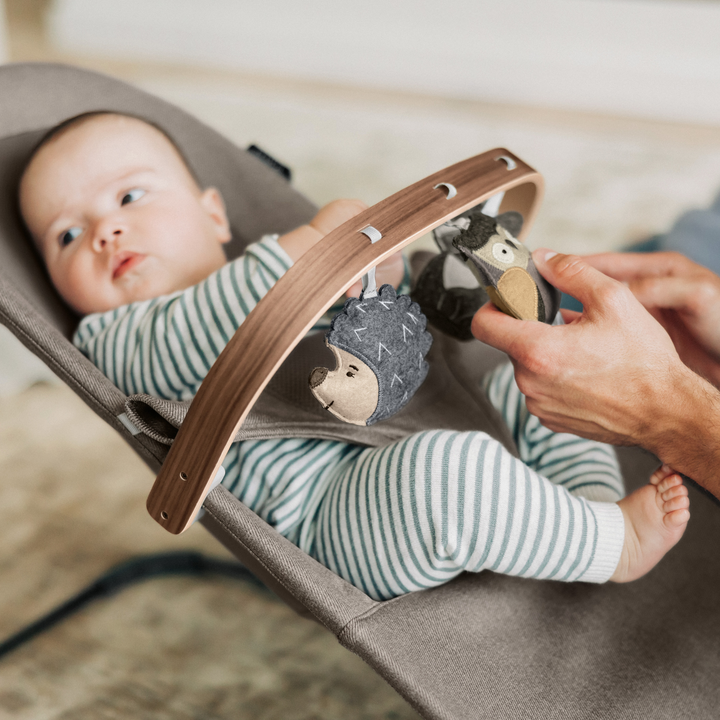 This is a lifestyle shot of the forest fun toy bar in use on a bouncer with a baby