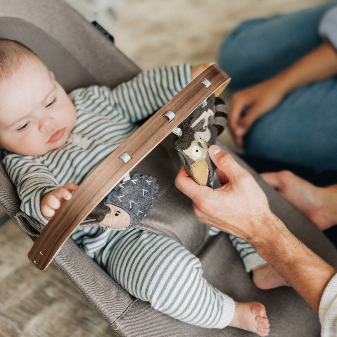 This is a lifestyle shot of a parent showing the forest fun bar to the baby in the bouncer