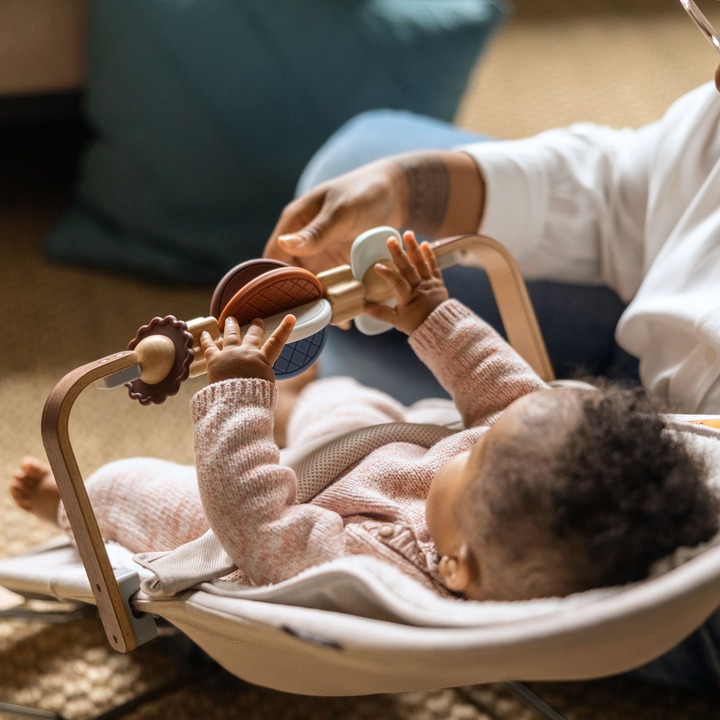 This is a lifestyle image of a baby playing with the wonder wheel toy bar with their parent while in the bouncer