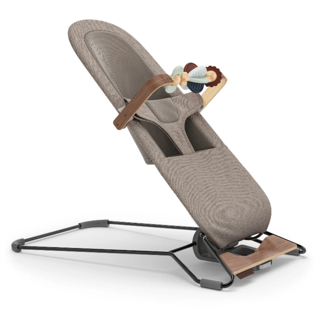 UPPAbaby Mira bouncer in a neutral beige fabric with the UPPAbaby Mira Wonder Wheel wooden toy bar attached, featuring sensory spinning toys and modern minimalist design on a sturdy black metal frame.