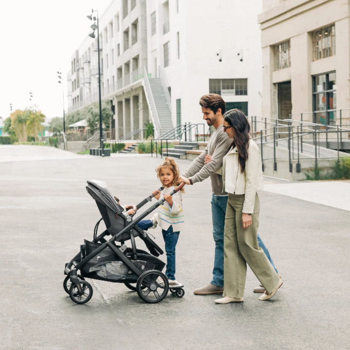 Family using UPPAbaby Vista V3 stroller with PiggyBack ride-along board, toddler standing while baby rides