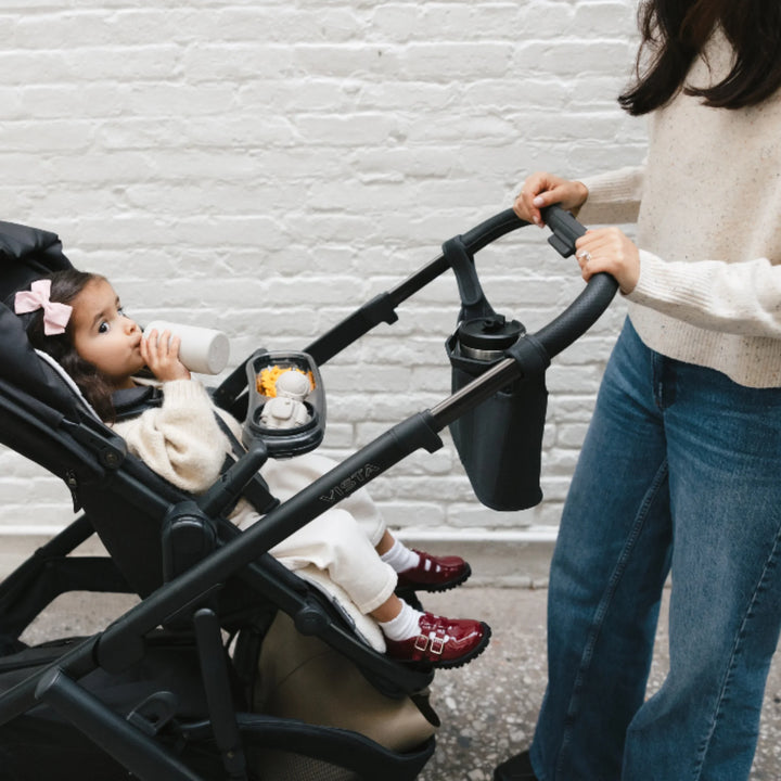 UPPAbaby Vista V3 stroller in Jake with Carry-All Parent Organiser and Snack Tray, child seated and drinking from bottle.
