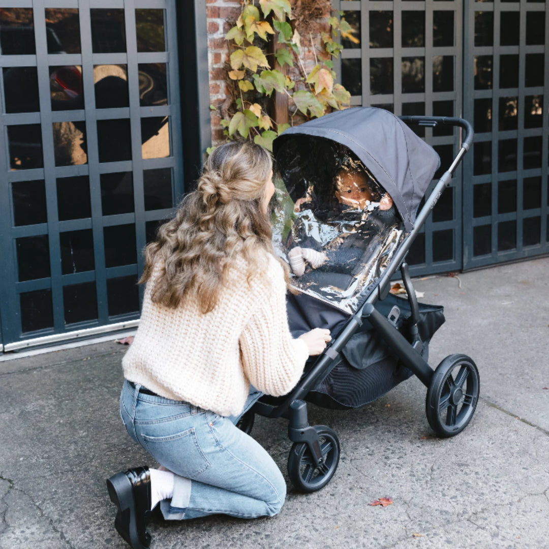 UPPAbaby Vista V3 stroller with Performance Rain Shield closed, showing parent checking on child under the canopy for full rain and wind protection.
