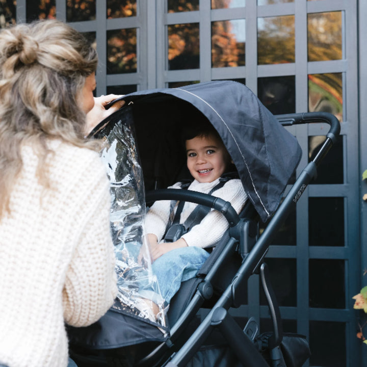 Parent opening UPPAbaby performance rain shield on Vista V3 stroller seat, keeping toddler dry and protected outdoors.
