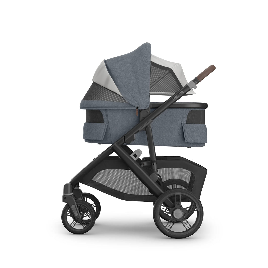 Side view of the UPPAbaby Vista V3 stroller in Jullian blue with the newborn bassinet canopy fully unzipped to reveal the ventilated mesh panel, showcasing airflow design, extendable sunshade, adjustable handlebar, all-terrain wheels and spacious under-seat storage basket on the premium Vista travel system