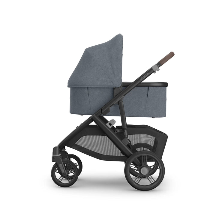 Side view of the UPPAbaby Vista V3 stroller in Jullian blue with newborn bassinet attached, showcasing the extended canopy, leather-accented handlebar, large all-terrain wheels and spacious mesh storage basket on the premium Vista travel system