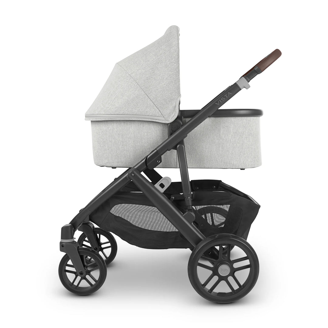 Side profile of UPPAbaby Vista V2 Anthony pram with carrycot in light grey fabric, featuring black frame, brown leather handlebar, and large storage basket — award-winning baby travel system designed for newborn comfort and style