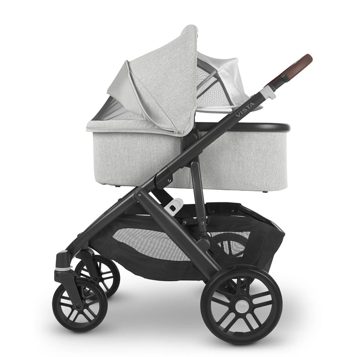 Side view of UPPAbaby Vista V2 Anthony travel system with carrycot in light grey fabric, featuring black frame, brown leather handle, and large storage basket — premium newborn pram and pushchair combination for modern families.