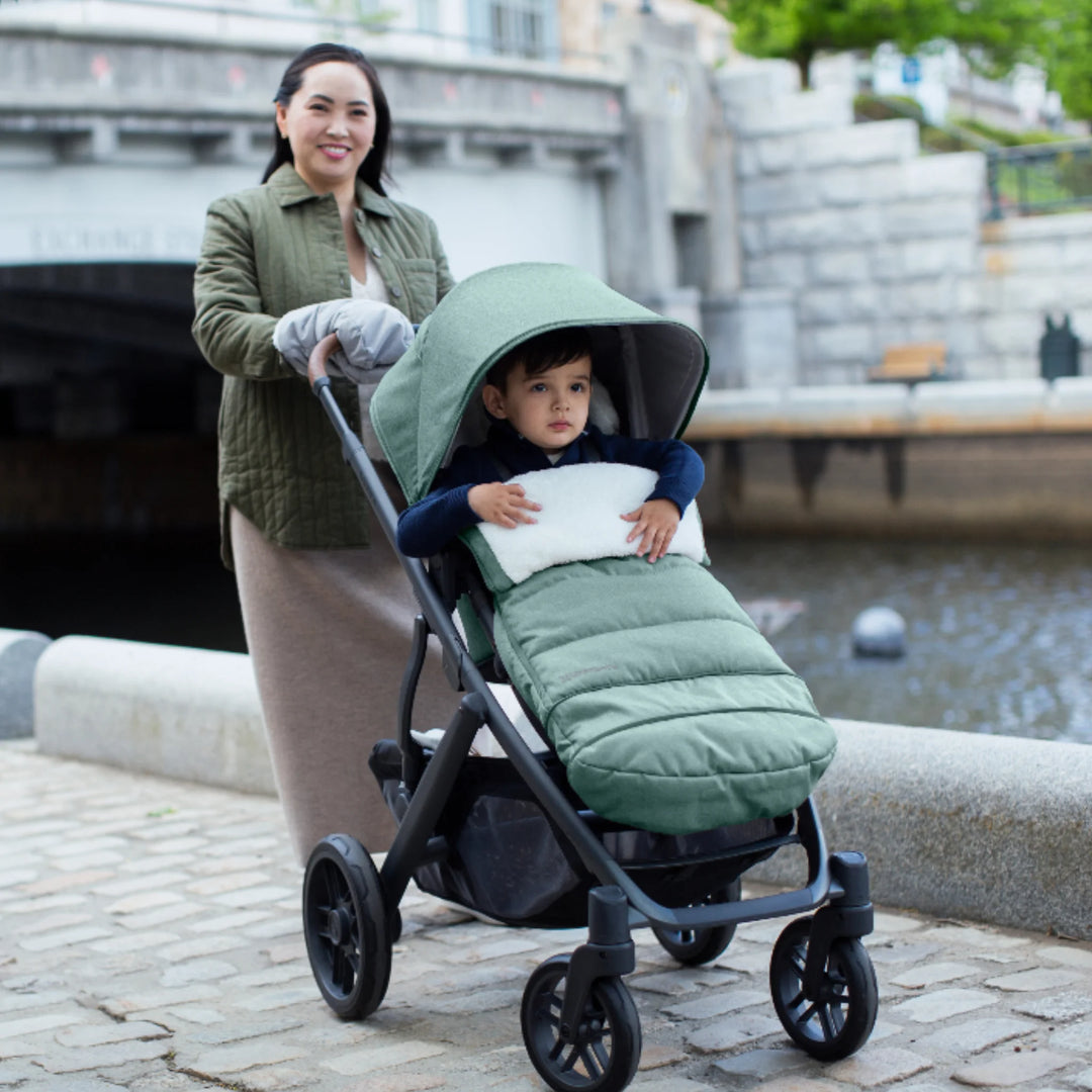 UPPAbaby CozyGanoosh footmuff in Gwen green used on a stroller, keeping a toddler warm and comfortable during an outdoor walk, with a weather-resistant, insulated design ideal for cold weather.