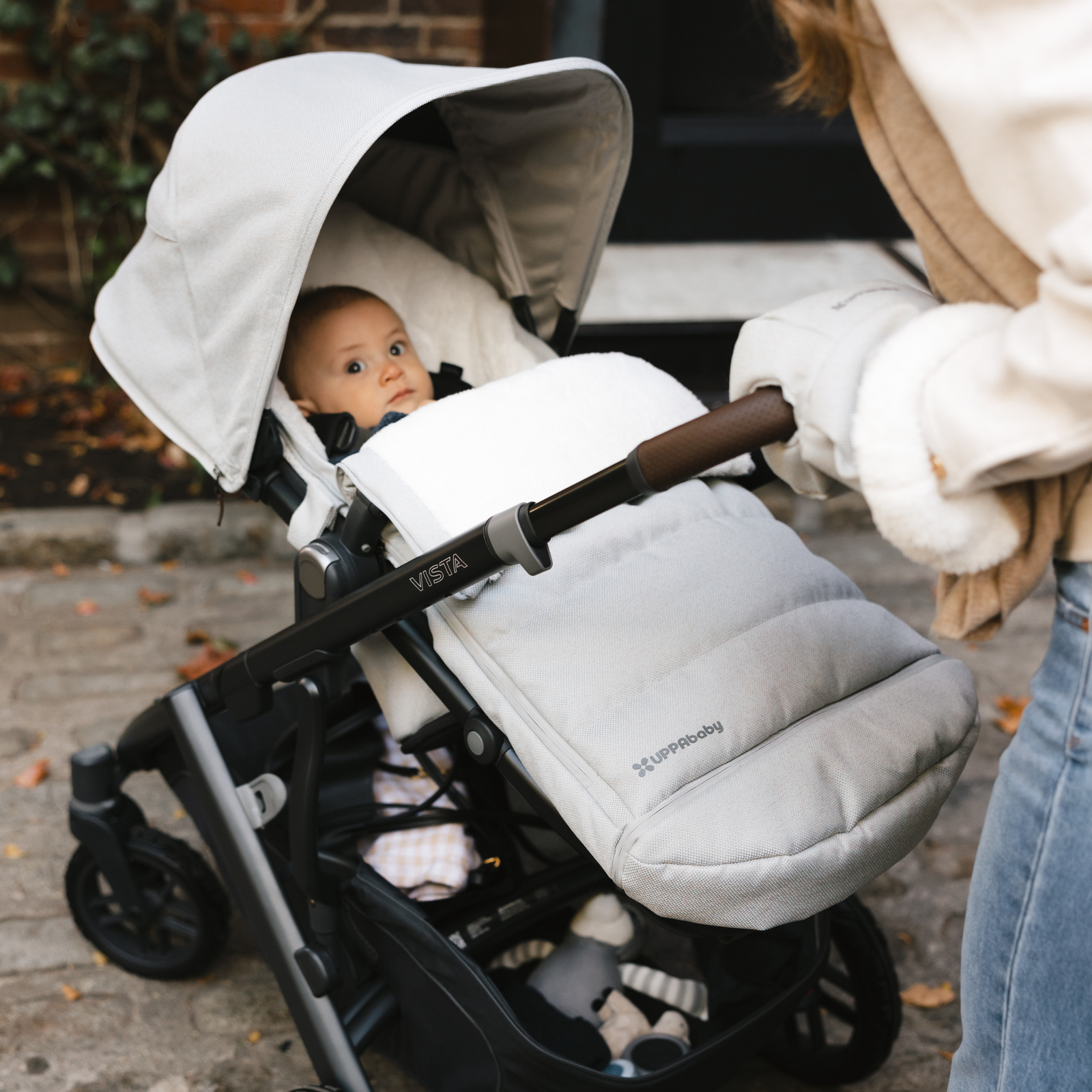 Baby seated in UPPAbaby VISTA V2 stroller in Declan Oatmeal, shown with cozy footmuff, extended canopy, premium leather handlebar, and padded seat for comfort and warmth – award-winning luxury pushchair for newborns and toddlers.