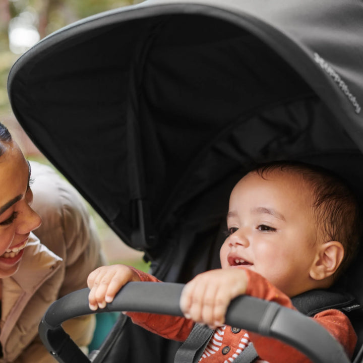 Toddler holding the UPPAbaby RIDGE stroller bumper bar under sun canopy on an outdoor walk