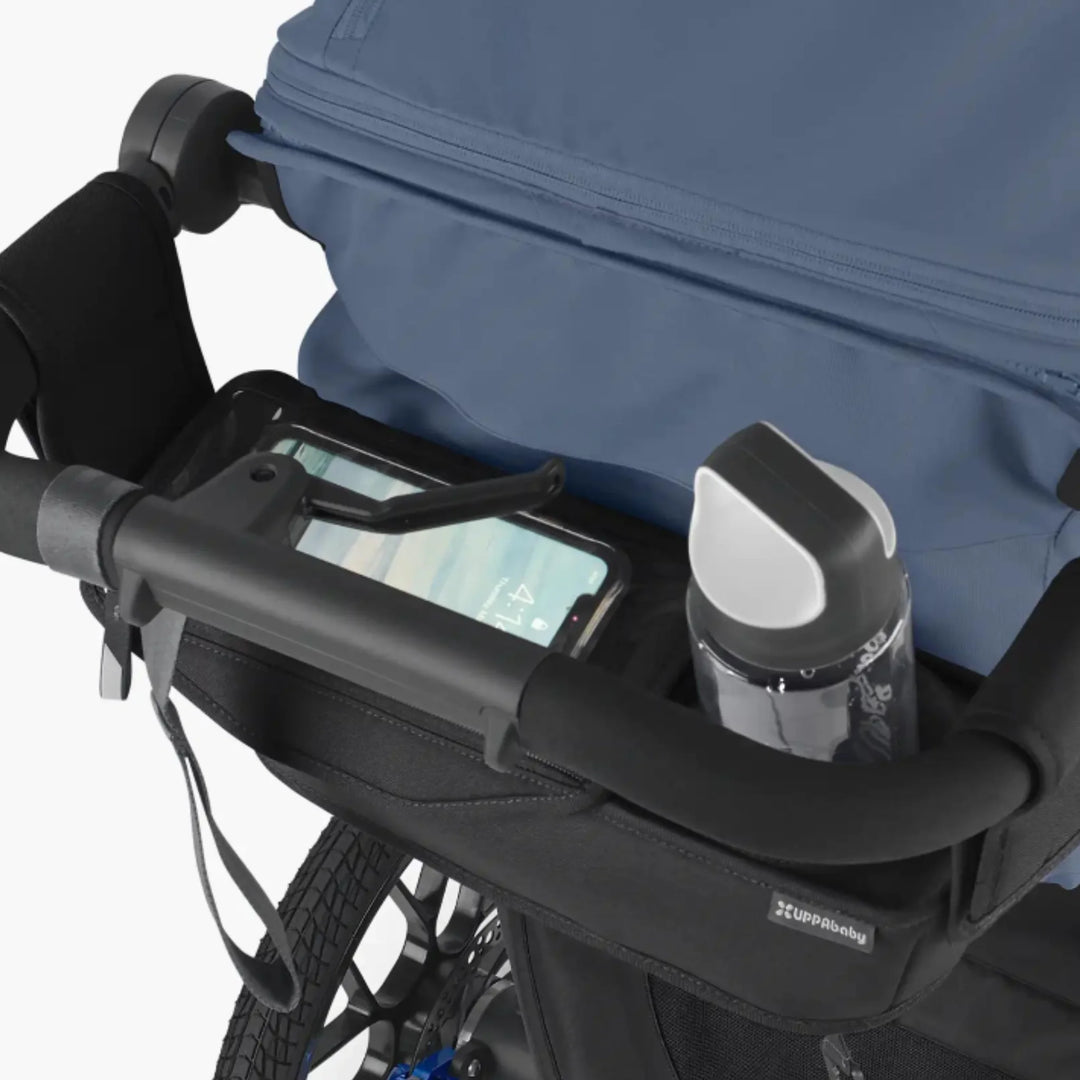 UPPAbaby RIDGE Parent Console stroller organiser with phone pocket and cup holder holding a water bottle, attached to stroller handlebar.