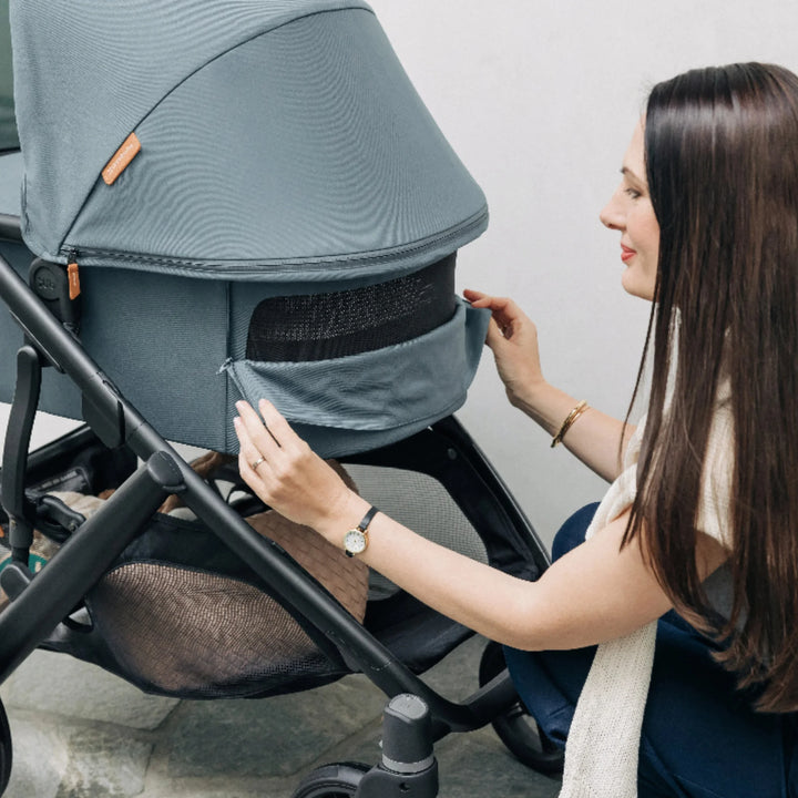 Mother adjusting the front ventilation panel on the UPPAbaby Vista V3 carrycot in the Dillian colourway, showing breathable mesh, premium fabric finish and sturdy stroller frame. Lifestyle image demonstrating airflow, comfort and functionality of the Vista V3 pram for newborns.