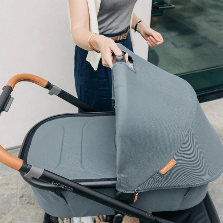 Parent lifting the UPPAbaby Vista V3 carrycot in the Dillian colourway using the easy one-hand release button, showcasing the ergonomic leather handlebar, premium canopy fabric and sturdy Vista frame. Lifestyle image highlighting the convenience, quality and functionality of the Vista V3 newborn carrycot system.