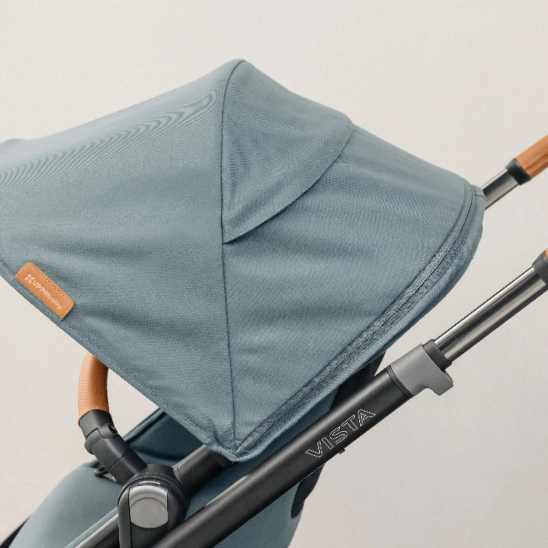 Close-up lifestyle image of the UPPAbaby Vista V3 stroller in the Dillian colourway, highlighting the premium textured canopy fabric, stitched branding tag, and extendable leather-accented handlebar on the Vista frame. Showcases high-quality materials and craftsmanship of the Vista V3 pushchair.