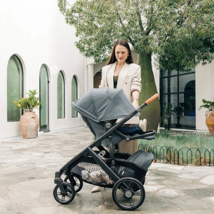 Mother pushing the UPPAbaby Vista V3 stroller in the Dillian colourway outdoors, with the toddler seat reclined and sun canopy fully extended. Lifestyle image showcasing the Vista V3’s premium leather handlebar, large all-terrain wheels, spacious storage basket and comfortable reclined seating for toddlers.