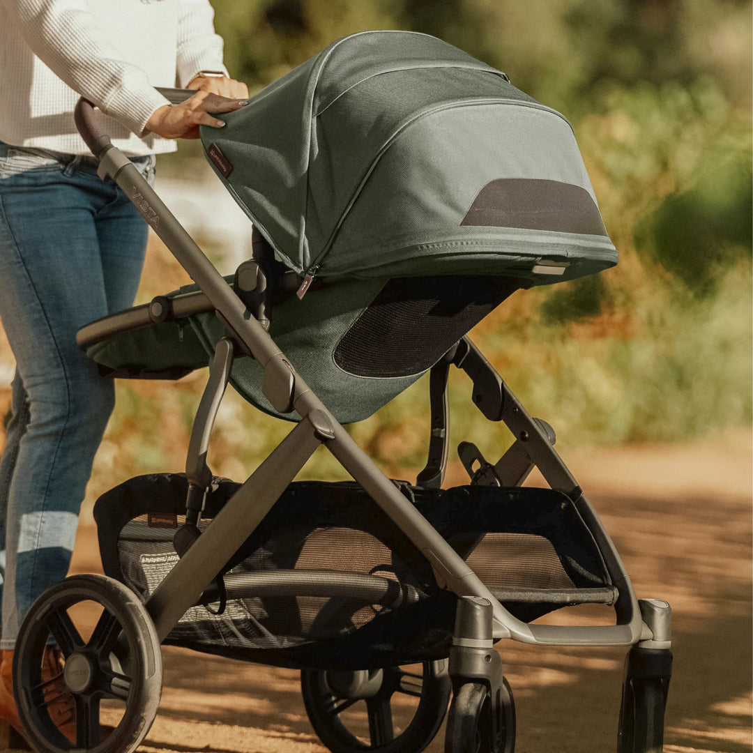Close-up of the UPPAbaby Vista V3 stroller in the Evelyn green colourway being pushed outdoors, highlighting the extended canopy, mesh ventilation, all-terrain wheels, sturdy suspension and spacious under-seat storage basket.