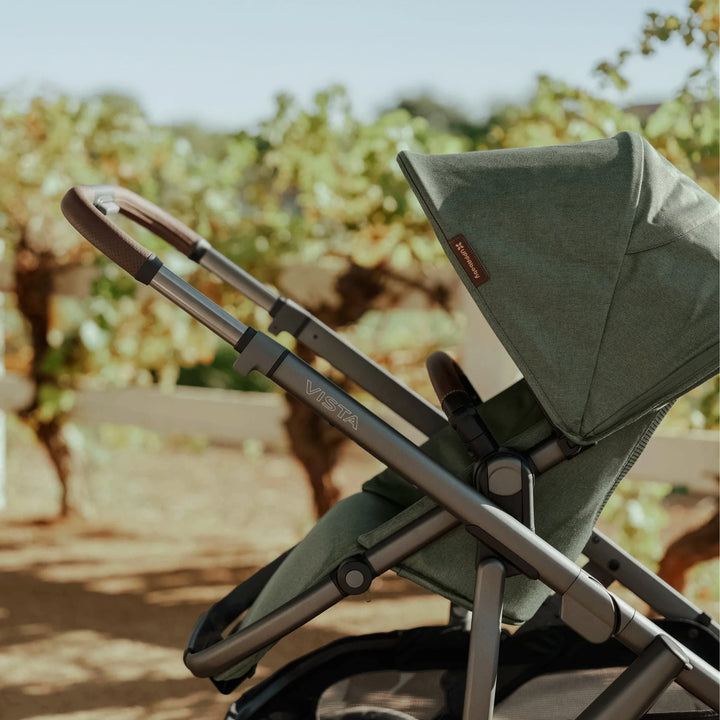 Side view of the UPPAbaby Vista V3 stroller in the Evelyn green colourway outdoors, highlighting the premium extendable canopy, sleek aluminium frame, leather-accented handlebar, and ergonomic seat design.