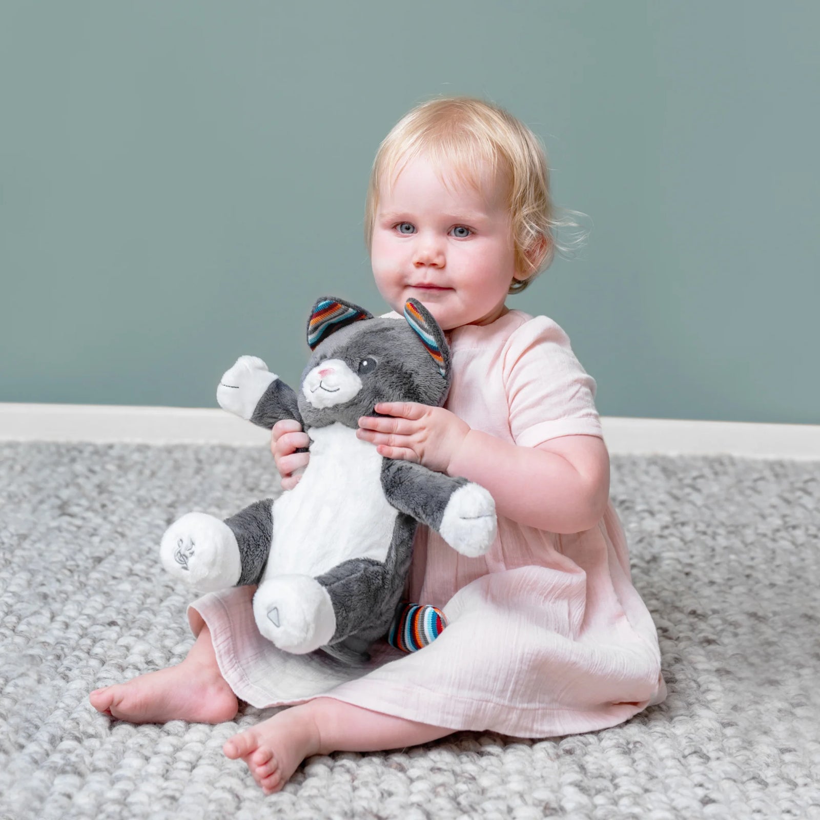 Child holding a plush toy on a carpeted floor with a plain background
