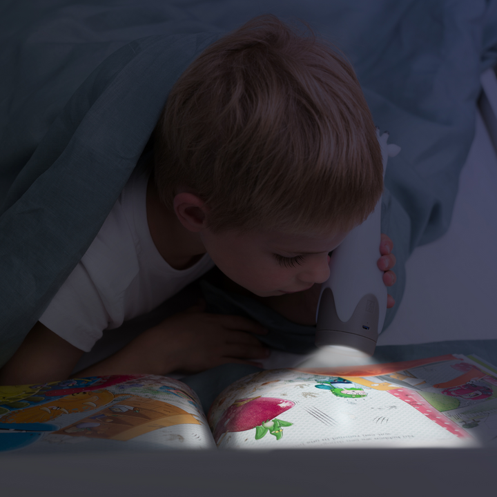 A child reading a book under their duvet cover using the light from the Gina the Giraffe torch feature.