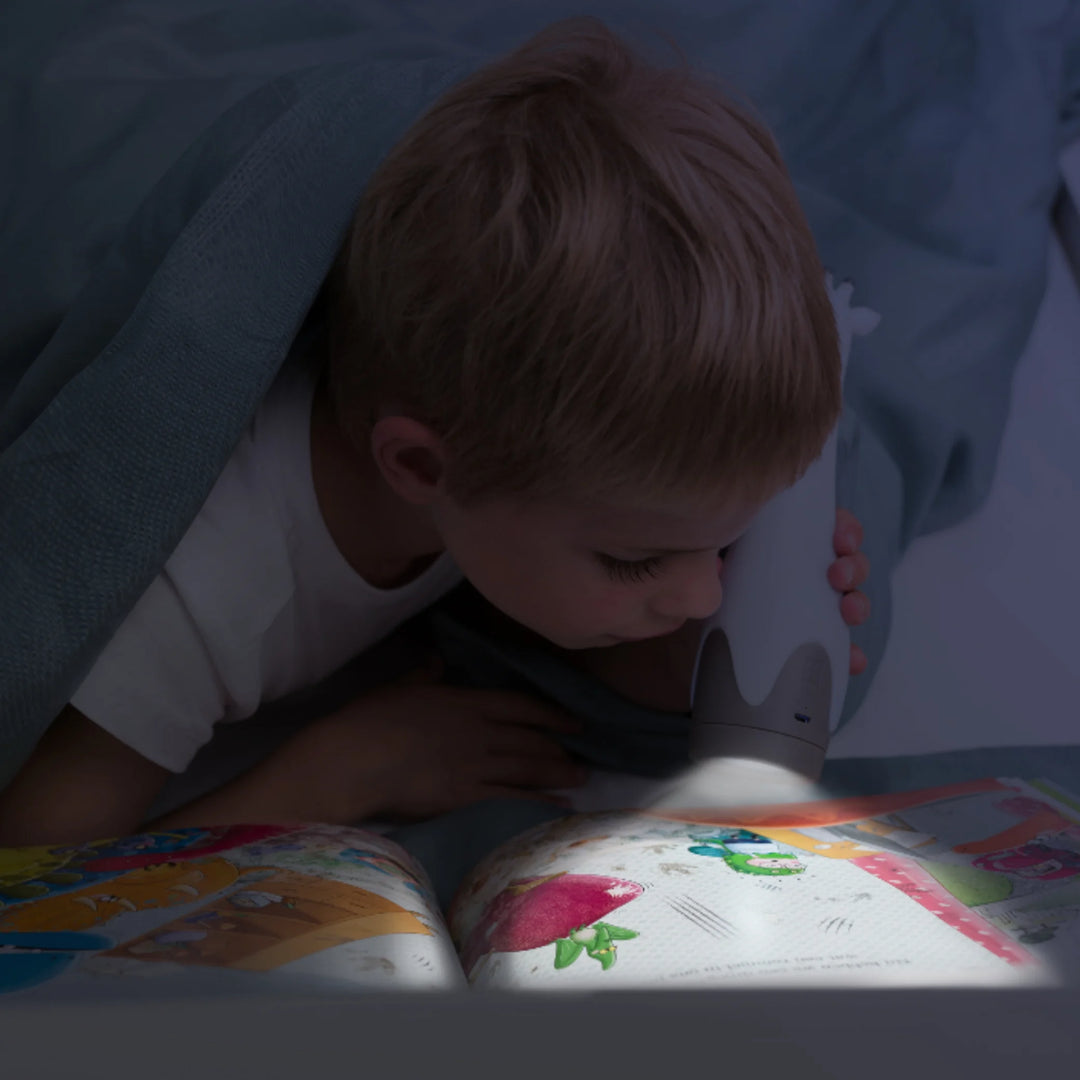 Child holding the glowing ZAZU Gina the Giraffe nightlight in a dimly lit bedroom.