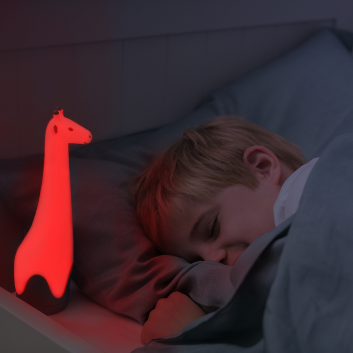 A child asleep in their bed with the Gina the Giraffe Nightlight mode on with a red colour setting.