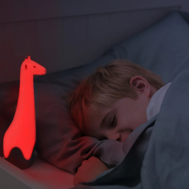 Child sleeping in bed beside the glowing red ZAZU Gina the Giraffe nightlight.