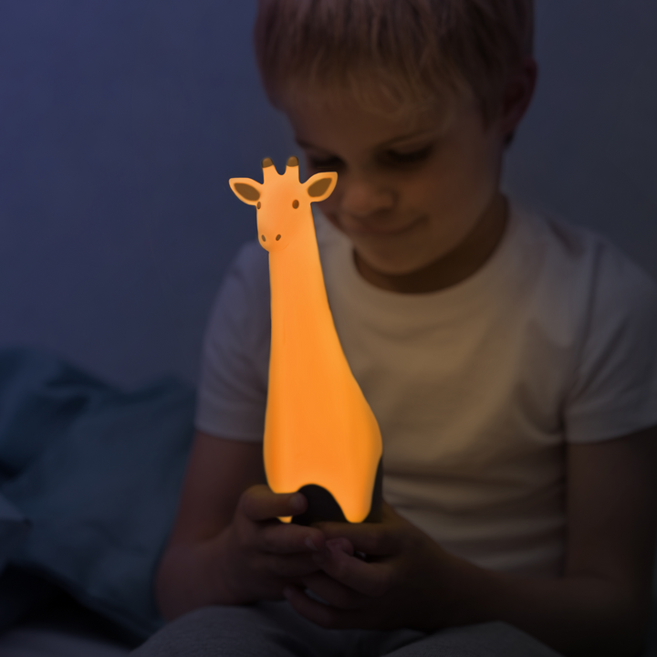 A child sitting on the edge of their bed holding the Gina the Giraffe Nightlight and changing the colour to yellow.