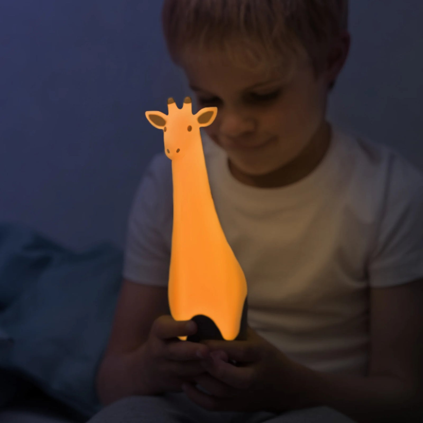 Child holding the glowing ZAZU Gina the Giraffe nightlight in a dimly lit bedroom.