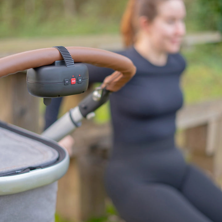 Parent relaxing outdoors with stroller using ZAZU Robby the Rocker baby rocker attached to the handle — portable automatic pram rocker that gently soothes babies to sleep while offering hands-free convenience for parents.