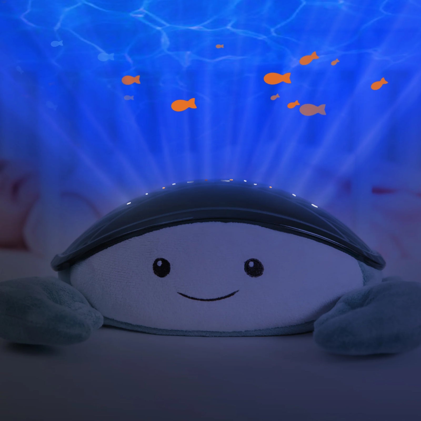 Zazu Cody Ocean Projector creating soothing underwater light effects beside a baby in a crib, projecting moving fish and calming blue waves to help babies relax and fall asleep peacefully.
