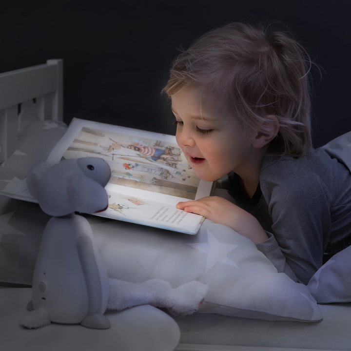 Little girl reading bedtime story by the soft glow of ZAZU Fin the Sheep Nightlight — calming children’s nightlight creating a cozy bedtime atmosphere, perfect sleep aid and reading companion for toddlers and kids’ bedrooms.