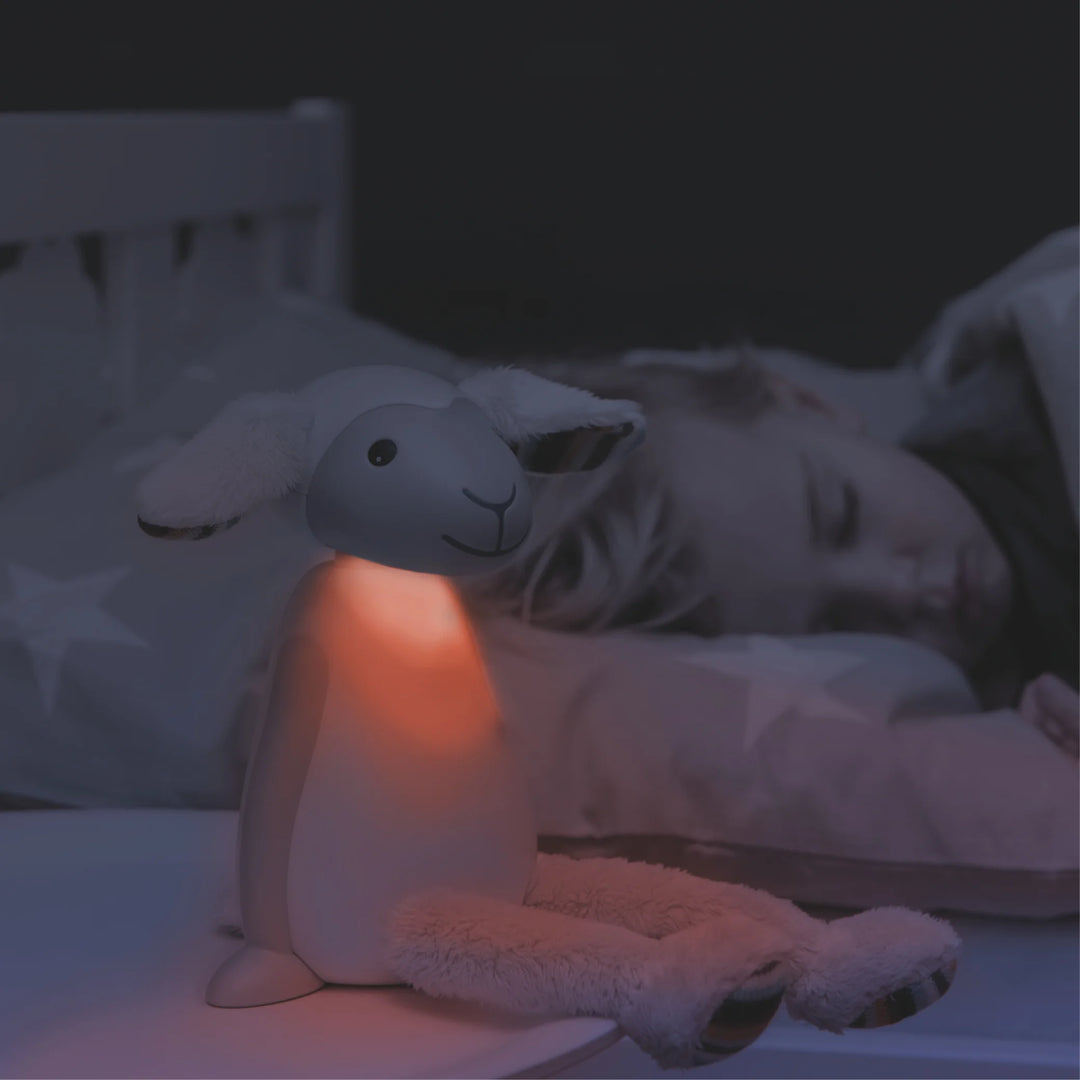 ZAZU Fin the Sheep Nightlight glowing red beside sleeping child — comforting kids’ bedside lamp with warm light to promote relaxation, peaceful sleep, and nighttime security in children’s bedroom.