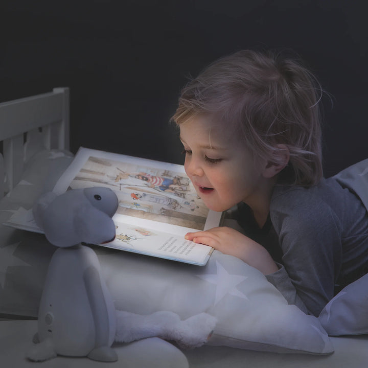 Child reading bedtime story illuminated by ZAZU Fin the Sheep Nightlight — soft LED kids’ night lamp providing gentle light for reading, relaxation, and peaceful bedtime routine.