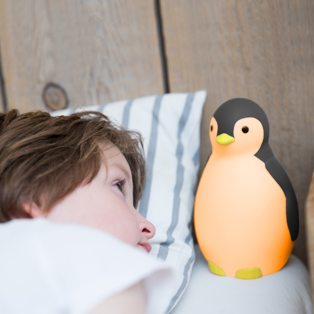 Child waking up beside Zazu Pam the Penguin Sleep Trainer glowing orange night light – children’s sleep training clock that signals when it’s time to wake up with color-changing lights and soothing sounds. Perfect bedtime aid for toddlers and preschoolers.