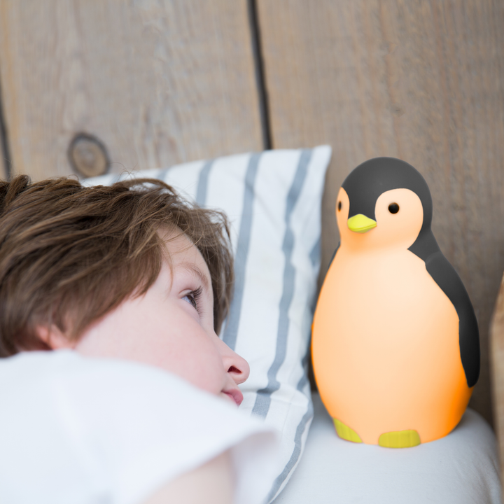 Child waking up beside Zazu Pam the Penguin Sleep Trainer glowing orange night light – children’s sleep training clock that signals when it’s time to wake up with color-changing lights and soothing sounds. Perfect bedtime aid for toddlers and preschoolers.
