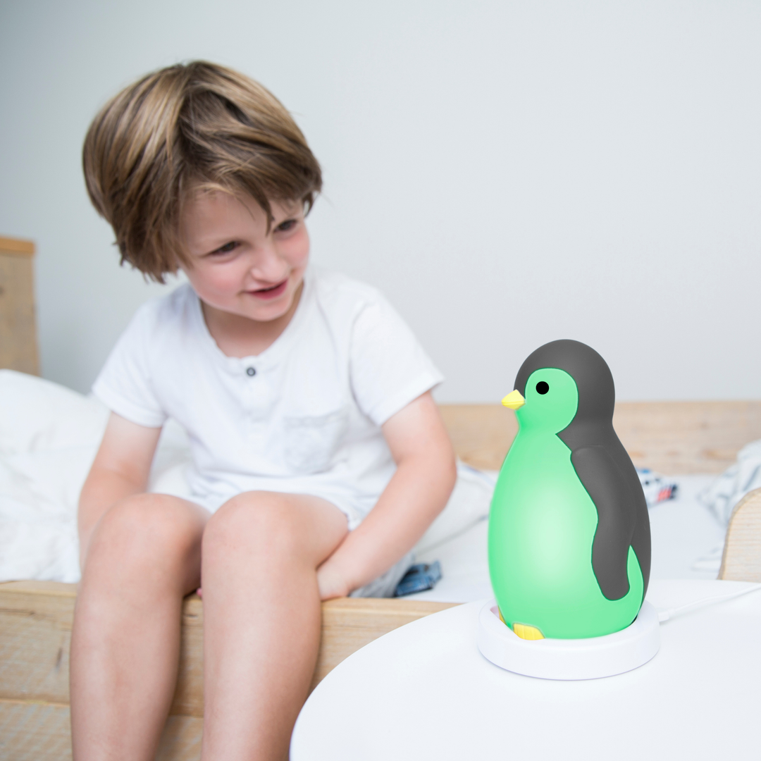 Child smiling at Zazu Pam the Penguin Sleep Trainer glowing green night light – children’s sleep training clock that shows it’s time to wake up with color-changing lights and soothing melodies. Fun and educational sleep aid for toddlers and young kids.