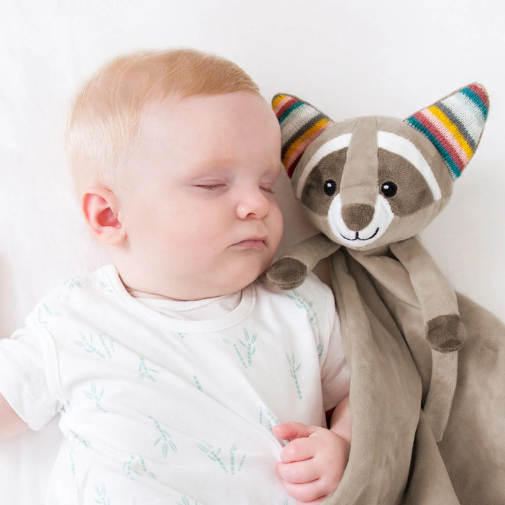 Sleeping baby cuddling the ZAZU Robin raccoon baby comforter — soft plush security blanket designed to soothe and support infant sleep.