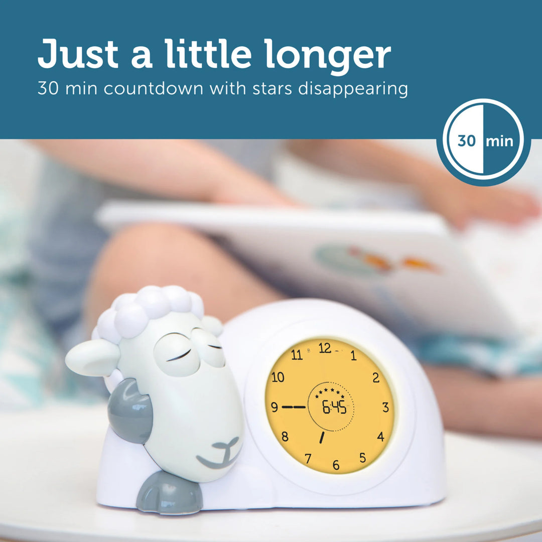 ZAZU Sam the Sheep sleep trainer clock in yellow countdown mode with sleepy sheep character, shown beside a child reading, demonstrating the 30-minute star countdown feature.