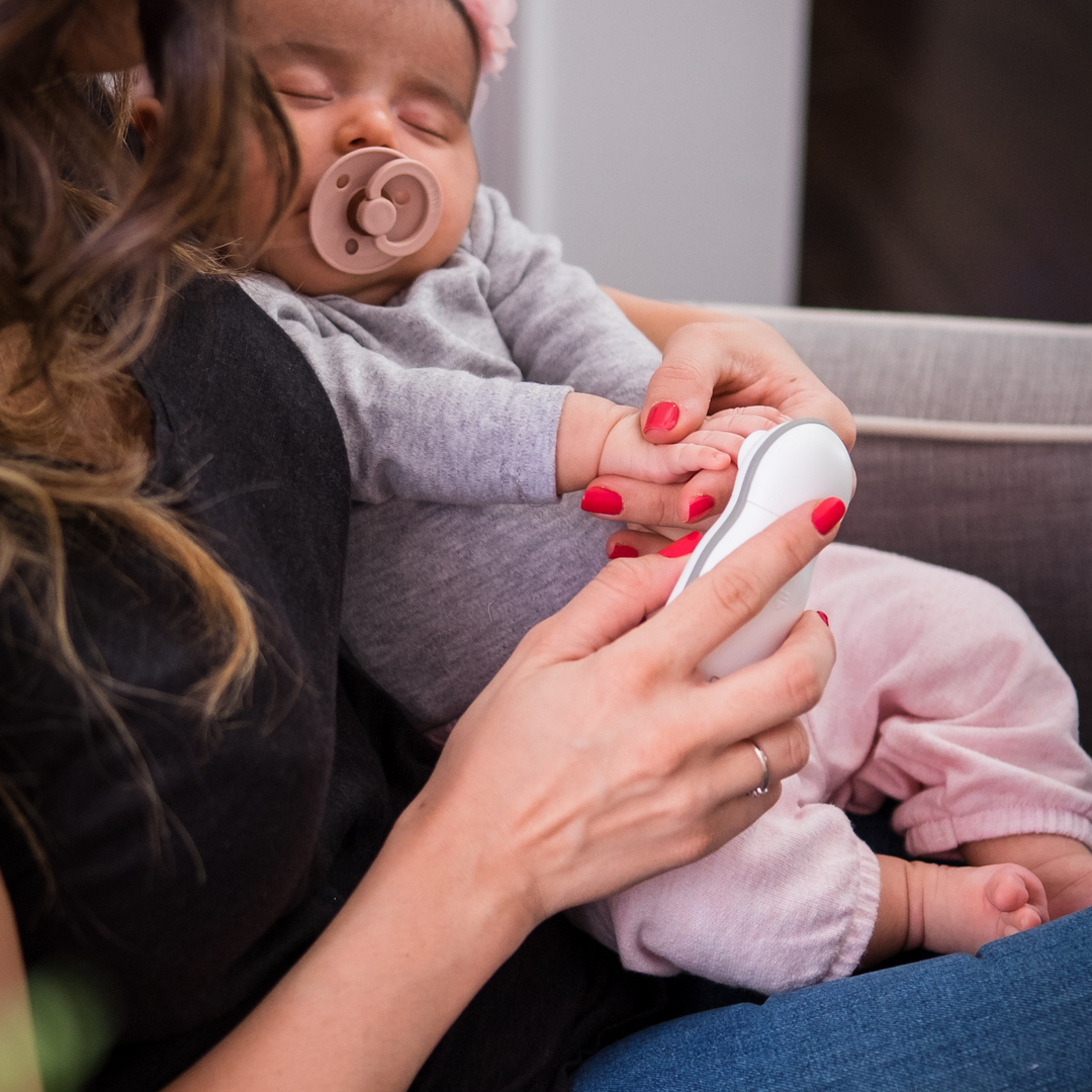 BBluv Trimo electric nail trimmer being used by a mother to file her sleeping baby's fingernails.