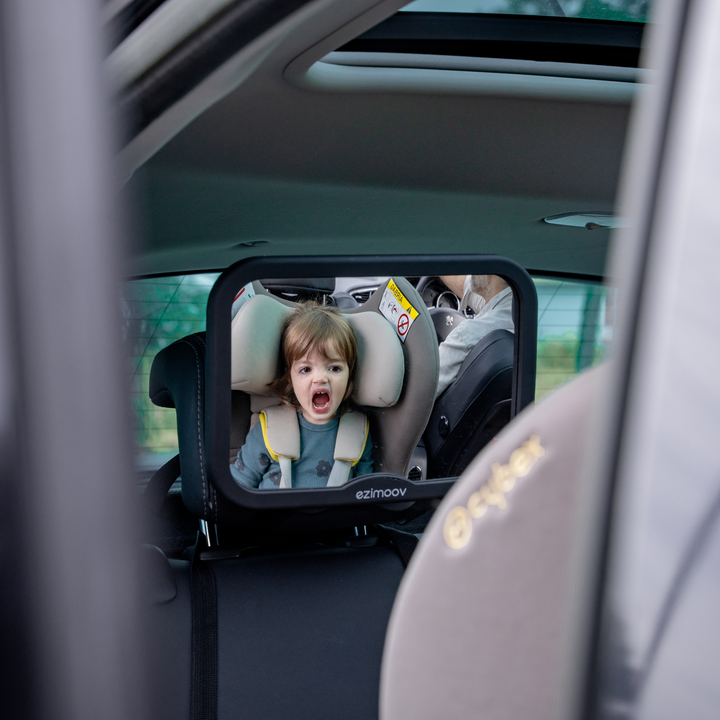 This image shows a child looking at their reflection in the mirror as they are in a rear facing car seat.